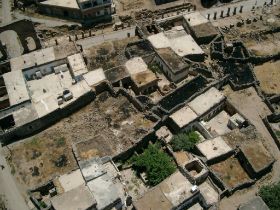 Bosra, links boven de boog en straat, en de huizen door de archeologische opgraving heen.jpg